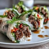 Thai Basil Beef Rolls on a platter with shredded carrots and cucumbers wrapped in soft translucent rice paper.