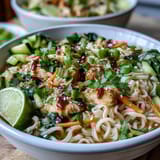 A hearty Asian Chicken Noodle Bowl topped with crisp vegetables, sesame seeds, and a drizzle of tangy sauce for bold flavor.  