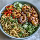 Succulent grilled shrimp atop sesame noodles, garnished with julienned carrots, cucumber, and cilantro in a quick Asian-inspired meal.
