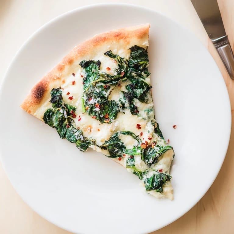 Close-up of a thin-crust spinach ricotta pizza topped with creamy ricotta and sautéed spinach.  