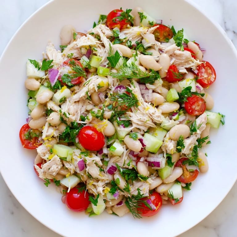 Freshly prepared Lemony White Bean Chicken Salad showcases bright cherry tomatoes, diced red onion, and fragrant dill on a rustic wooden table.