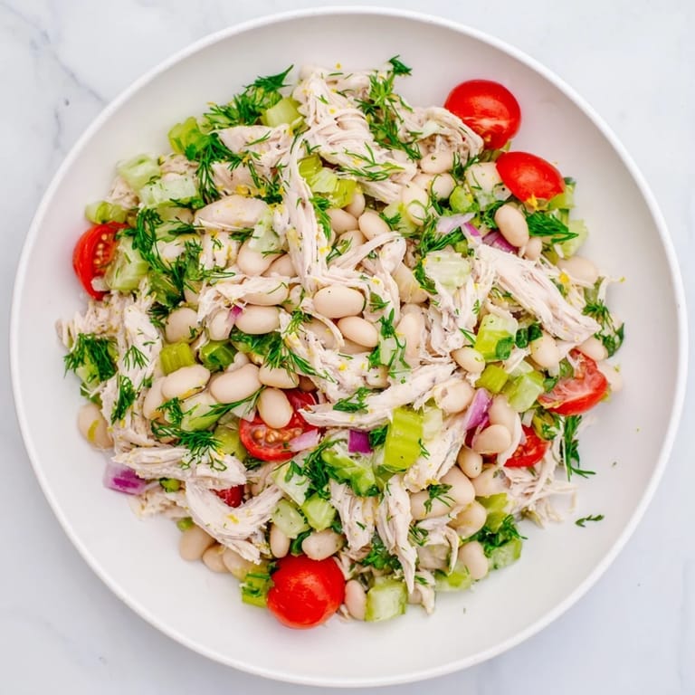 A close-up of Lemony White Bean Chicken Salad glistening with olive oil and lemon zest, garnished with chopped parsley and black pepper.