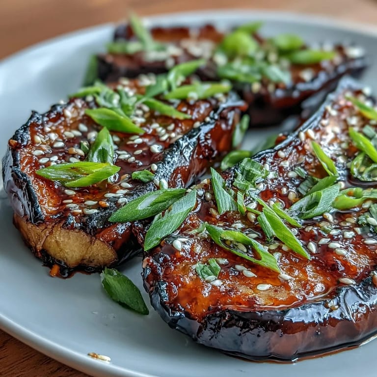 Tender roasted miso glazed eggplant brushed with sweet-savory glaze, steaming slightly on a white plate ready for a Japanese-inspired meal.
