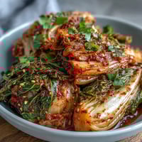 Vibrant red kimchi packed tightly in a glass jar, showcasing fermented napa cabbage and crunchy daikon radish slices glistening with spicy chili paste.  