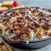 Gooey smores dip with melted chocolate and toasted marshmallows in a cast iron skillet, perfect for 4th of July celebrations.