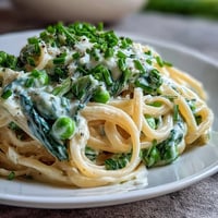 Spring pasta with lemon cream sauce and peas, garnished with fresh chives and Parmesan cheese, in a white bowl.